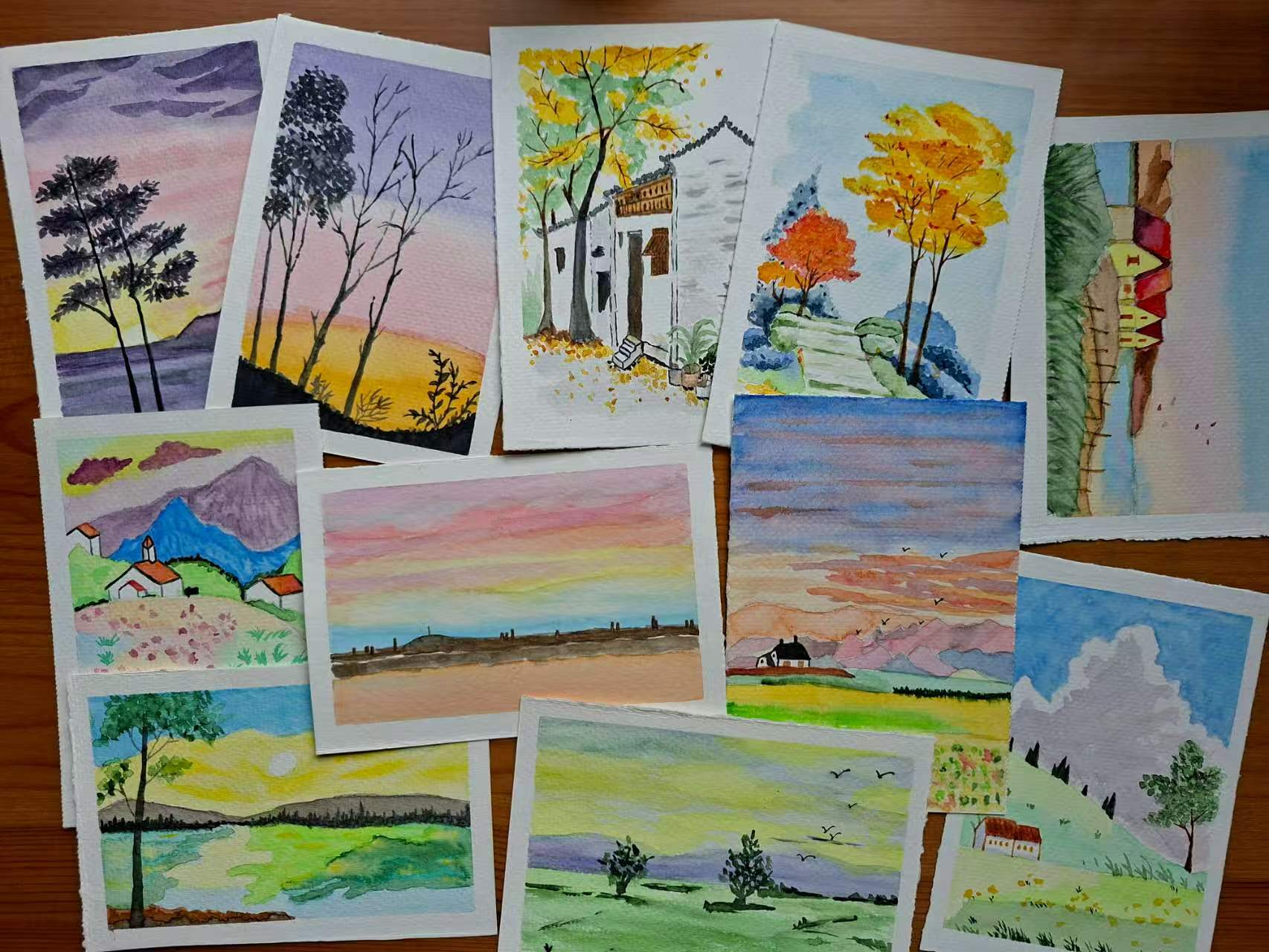 Original watercolour paintings of trees, landscapes and buildings arranged on a wooden table